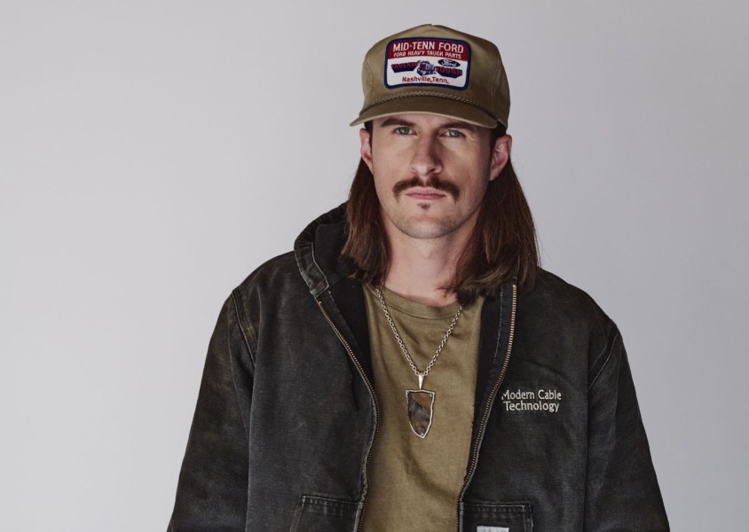 John Morgan wearing a green tshirt, black jacket, and green capx